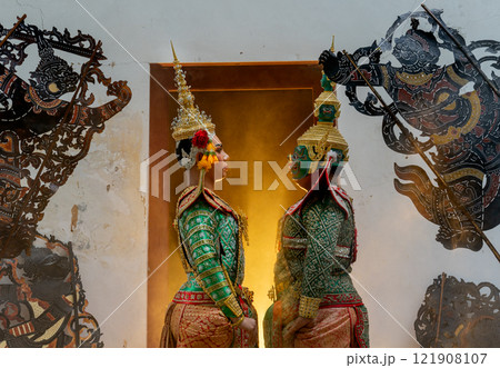 Two charactor of Khon mask costume as angel and giant stand with facing each other in front of door frame with warm light in the back. Two charactor of Khon mask costume as angel and giant stand with facing each other in front of door frame with warm light in the back. 121908107