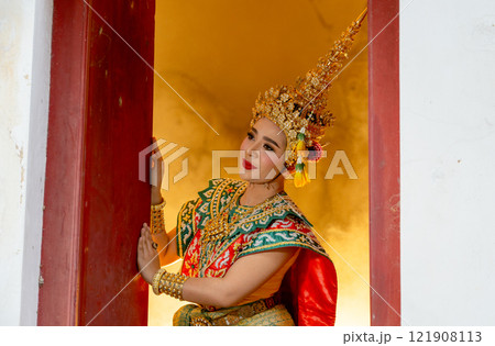 Woman with Khon mask charactor as angel stand in front of door frame of old building and look to her right side with warm light in the background. 121908113