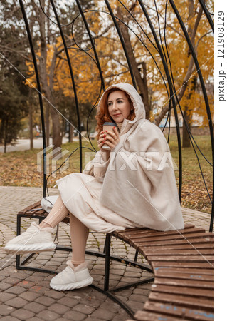 Woman Autumn Park Beige Poncho: Enjoying Coffee Outdoors Fall Day Relaxing Cozy Outfit. 121908129