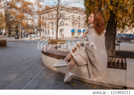 Woman Autumn City Park Bench: Elegant lady sits stylishly on a park bench during autumn in a city. 121908151