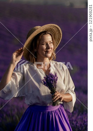 A woman wearing a straw hat and holding a bunch of lavender flowers 121908281