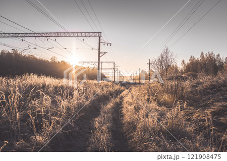 Suburban morning winter landscape of a railway station. The sun fills dry bushes and grass with soft golden light. Winter landscape of nature covered with frost 121908475