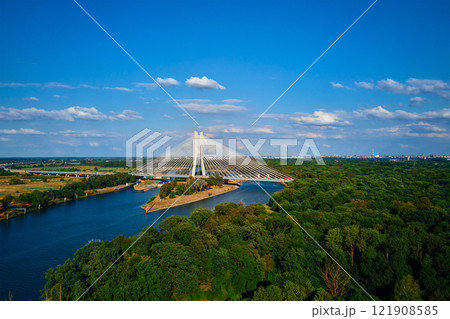 Cable stayed bridge over river surrounded by lush green forest. Redzinski bridge over Odra river with cars driving on highway in Wroclaw, Poland Cable stayed bridge over river surrounded by lush green forest. Redzinski bridge over Odra river with cars driving on highway in Wroclaw, Poland 121908585