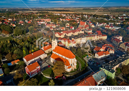 Aerial view of European town with colorful buildings and church at sunset. Suburban landscape with red roofed houses in small city surrounded by lush greenery and countryside fields 121908606