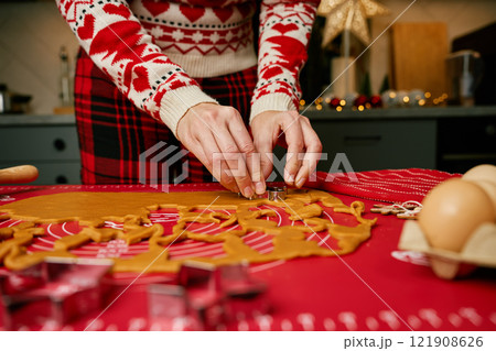 Woman in festive sweater using cookie cutters to shape gingerbread dough on red mat. Baking traditional Christmas cookies in home kitchen Woman in festive sweater using cookie cutters to shape gingerbread dough on red mat. Baking traditional Christmas cookies in home kitchen 121908626