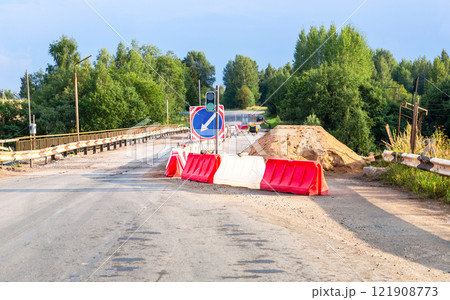 Repair work on a road bridge. A road sign indicating the direction of travel and a temporary traffic light to regulate traffic flow Repair work on a road bridge. A road sign indicating the direction of travel and a temporary traffic light to regulate traffic flow 121908773