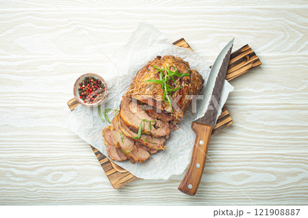 Rolled turkey roasted with spices and herbs on baking paper with knife and wooden white background top view. Baked cut for slices turkey fillet roll for dinner 121908887