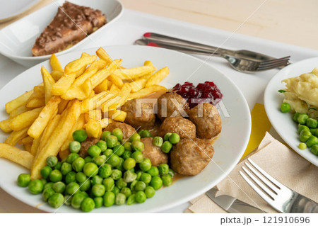 Meatballs with french fries, green peas, bechamel sauce and cranberry jam, meat balls on white plate 121910696