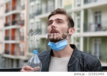 Young handsome man with medical protective mask on chin drank mineral water from a big bottle 121912403