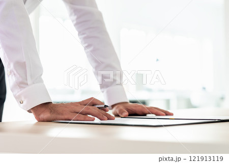 Businessman leaning on office desk to sign a document 121913119