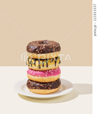 Stack of glazed donuts with different toppings on white plate on beige and white background. 121913337