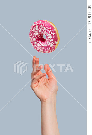 Hand with levitation glazed pink donut on blue background. 121913339