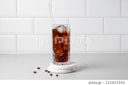 Cold brew coffee in a glass with ice on a light table against a white brick background Cold brew coffee in a glass with ice on a light table against a white brick background 121913342