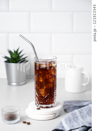 Cold brew coffee in a glass with ice and straw on a light table against a white brick background Cold brew coffee in a glass with ice and straw on a light table against a white brick background 121913343