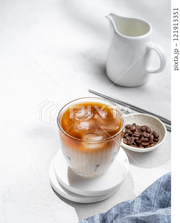 Iced coffee latte in a glass with milk on a light background with coffee beans 121913351