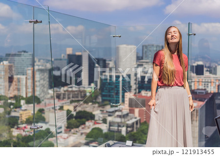 Female tourist or businesswoman standing on a skyscraper rooftop with a panoramic view of Mexico City. Travel or international business in Mexico concept 121913455