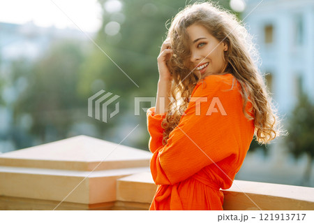 Young woman posing against backdrop of urban landscape in bright orange dress. Concept of lifestyle. Young woman posing against backdrop of urban landscape in bright orange dress. Concept of lifestyle. 121913717