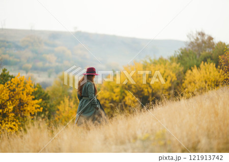 Beautiful stylish girl walks in the autumn park. The girl is dressed in a green coat and a red hat. Beautiful stylish girl walks in the autumn park. The girl is dressed in a green coat and a red hat. 121913742