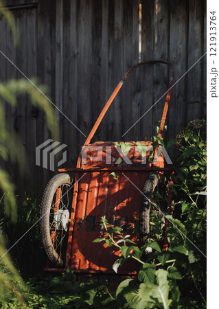 An old red wheelbarrow stands near an old wooden fence. 121913764