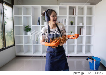 Joyful Woman Cleaning with Duster Wearing Headphones Joyful Woman Cleaning with Duster Wearing Headphones 121914447