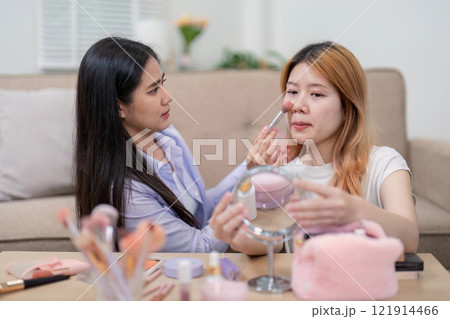 Asian woman assisting with blush application indoors 121914466