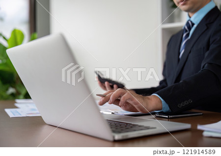 Businessman Working on Laptop with Calculator and Notes 121914589