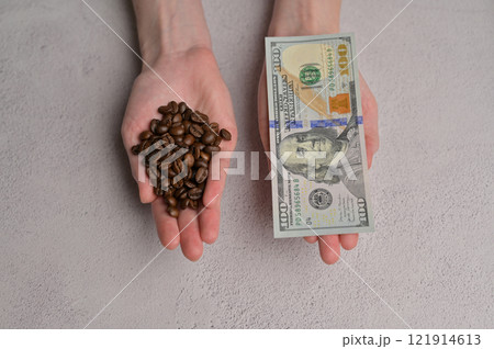Top view fresh aromatic grain coffee and 100 American dollars paper cash banknote in a woman's hands, white background. Rising coffee prices in the world 121914613