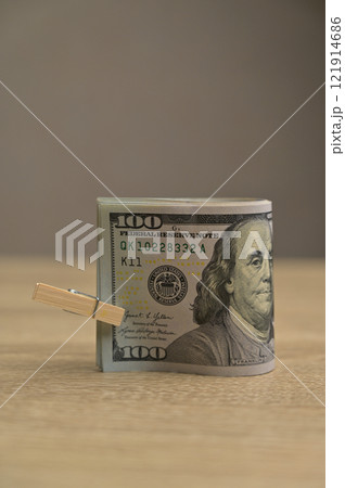 Roll of 100 American dollars paper cash banknotes with a small clothespin on a wooden table background, isolated Roll of 100 American dollars paper cash banknotes with a small clothespin on a wooden table background, isolated 121914686