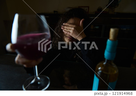 Woman with wine at table, covering face in dark, contemplative mood Woman with wine at table, covering face in dark, contemplative mood 121914968
