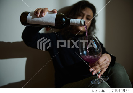 Woman pouring red wine into glass in a dimly lit room 121914975
