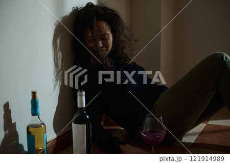 Woman sitting on floor near bottles and glass exhibiting dark emotions 121914989