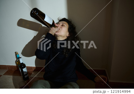 Woman Drinking From A Wine Bottle Sitting Against A Wall Woman Drinking From A Wine Bottle Sitting Against A Wall 121914994