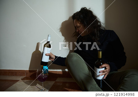 Woman sitting with wine bottles in dimly illuminated room Woman sitting with wine bottles in dimly illuminated room 121914998