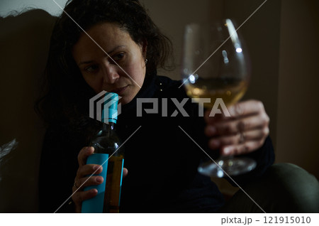 Woman holding a wine glass in contemplation inside a dimly lit room 121915010