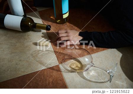 Scene of wine bottles, spilled glass, hand on tiled floor 121915022