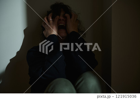 An individual showing despair seated in a dimly lit corner 121915036