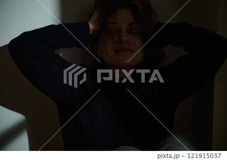 Woman distressed in low-light room holding her head 121915037