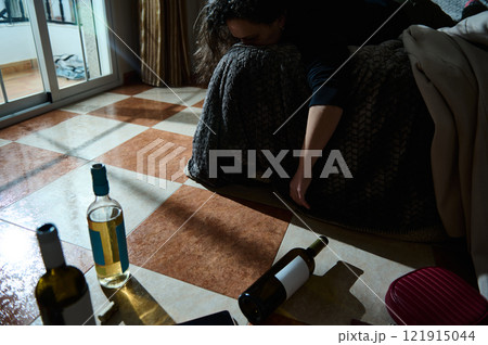 Person lying by scattered wine bottles in a dimly lit room 121915044