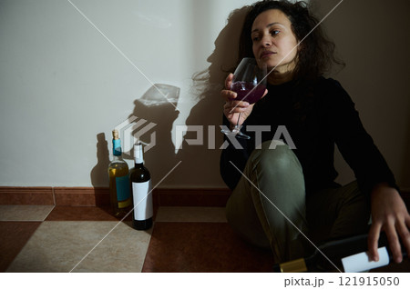 Woman sitting on the floor with wine bottles reflecting solitude and contemplation 121915050