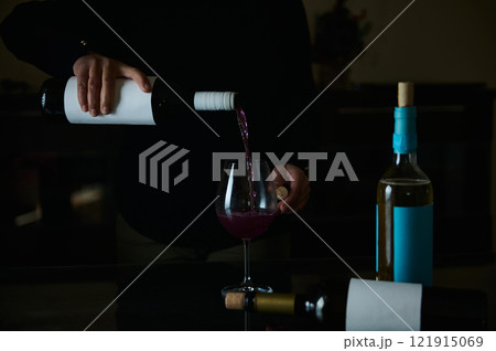 Pouring red wine into a glass with bottles arranged on a dark table Pouring red wine into a glass with bottles arranged on a dark table 121915069
