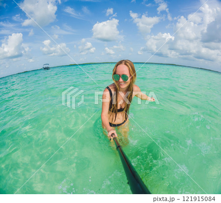Woman standing in the crystal-clear waters of Lake Bacalar, Mexico, enjoying the serene beauty of the landscape. Tranquil moment in nature, outdoor escape, and relaxation concept 121915084