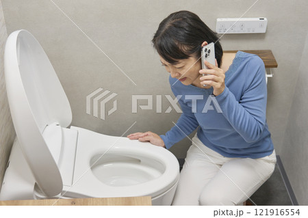トイレで修理業者に電話をする女性 トイレで修理業者に電話をする女性 121916554