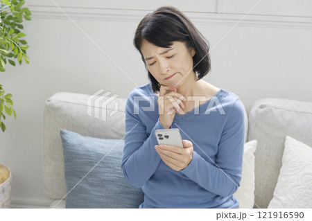 スマホを持って悩む中年女性　リビング 121916590