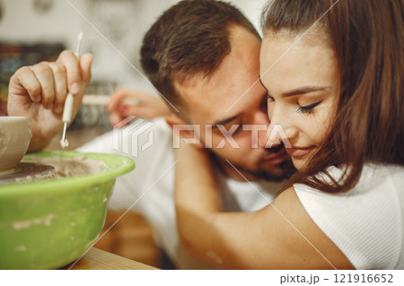 Mutual creative work. Young beautiful couple in casual clothes and aprons. People creating a bowl on a pottery wheel in a clay studio. 121916652