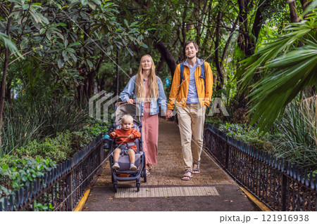 A married couple and their son in a stroller exploring lush streets of Condesa, Mexico City. Family adventure in a vibrant urban oasis. Travel, family bonding, and urban greenery concept in Latin 121916938