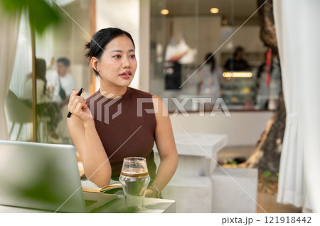 A thoughtful Asian woman looks away, pondering something while working remotely from a cafe. 121918442