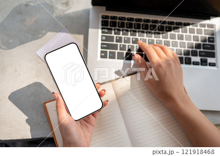Top view of a woman's hand holding a smartphone with a white screen mockup above a desk. Top view of a woman's hand holding a smartphone with a white screen mockup above a desk. 121918468