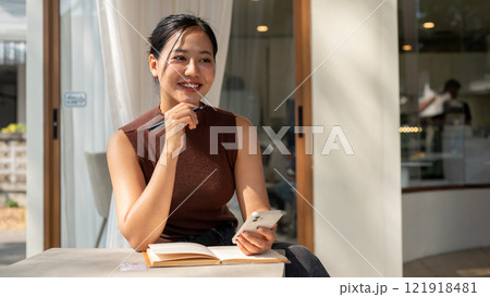 A smiling woman looks to the side, daydreaming and thinking about happiness while relaxing at a cafe A smiling woman looks to the side, daydreaming and thinking about happiness while relaxing at a cafe 121918481