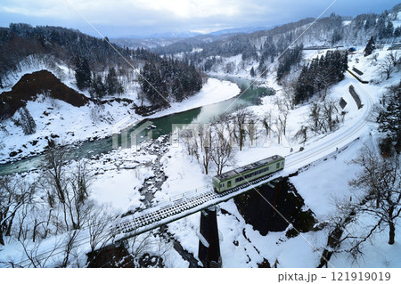 積雪の千曲川沿いの鉄橋を渡る飯山線のローカル列車 121919019