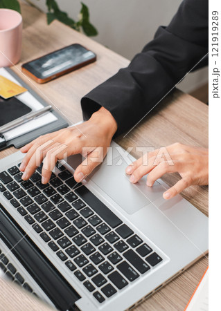 Business Professional Typing on Laptop at Wooden Desk with Smartphone and Office Supplies in Modern Workspace Business Professional Typing on Laptop at Wooden Desk with Smartphone and Office Supplies in Modern Workspace 121919289